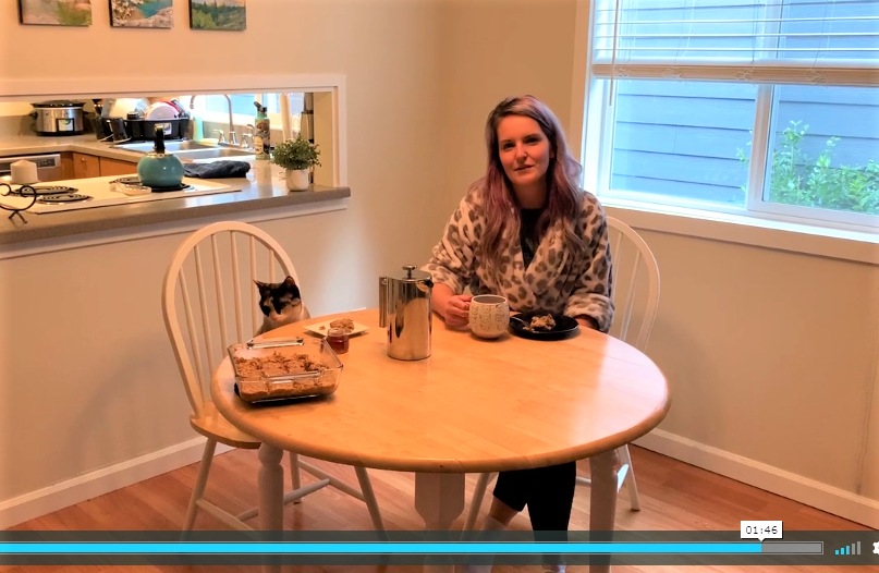 Virtual Breakfast A woman and a cat sit at a breakfast table with a pan of breakfast bars cooling on the table.