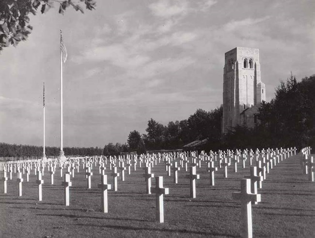 Greyscale photo of white chapel tower and cross-shaped gravestones
