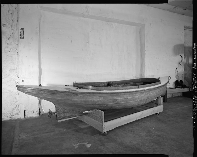 Black & white photograph of small metal & wood boat on a wooden stand