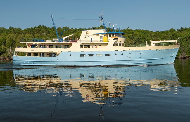 Starboard side of motor vessel Ranger III; a light blue and white ship on a lake with wooden island in background