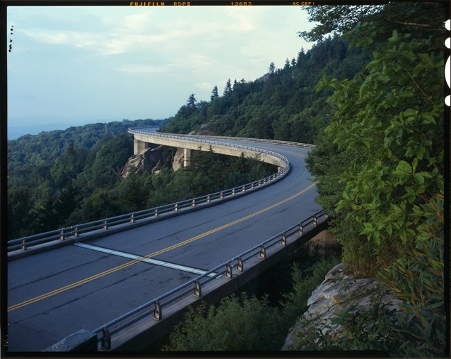 Road viaduct as it curves to the left around a green mountain