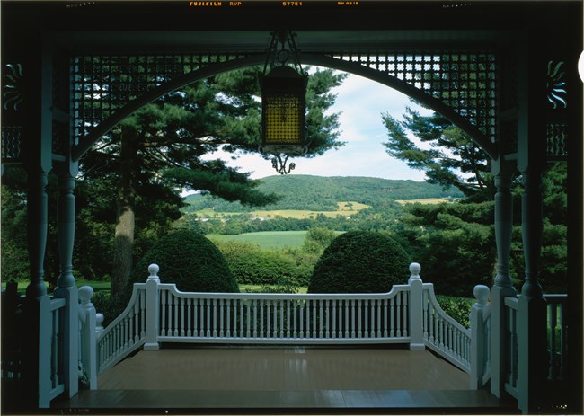 View from a white wooden veranda to green meadow, trees, and mountain