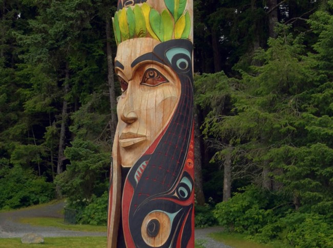 painted wooden totem pole with carvings of woman's face and salmon