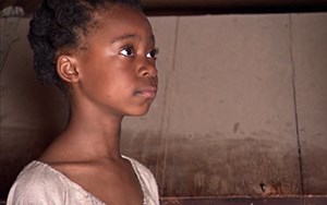 A young black girl wearing a white dress faces right