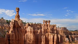 A red rock formation creates a canyon with various levels of geology showing underneath a blue sky with whispy clouds