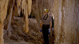 A ranger wearing a hard hat with a headlamp walks though a cave