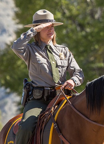 Jackie Sene, siting on a horse, wears her NPS uniform and flat hat as salutes an unseen flag.