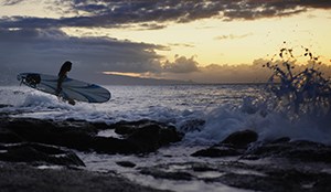 A person carrying a surfboard walks into the waves