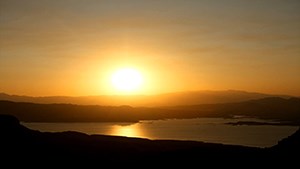 The sun creates a hazy glow over the horizon as its reflection is show in the water below