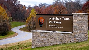 A brown wooden panel sign on a stone base for Natchez Trace Parkway