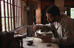 A black man leans over a work bench
