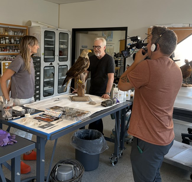 Man and woman around an eagle mount as a man films them on a camera