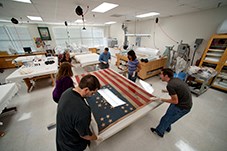 Conservators treating an American flag. Six people hold an American flag from the Civil War.