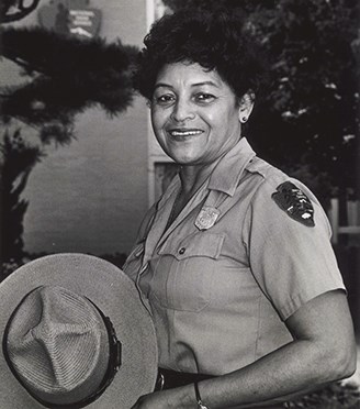 Maxine Boyd stands smiling in her NPS uniform, holding her wide-brimmed hat in her hands.