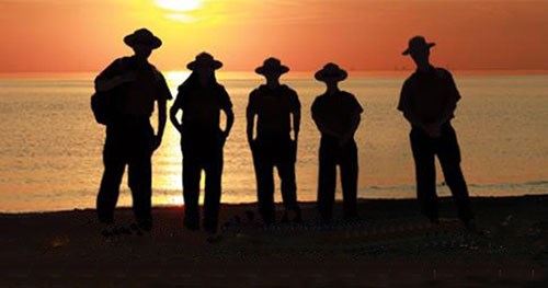 Five rangers wearing broad-brimmed flat hats in silhouette watching the sunset.