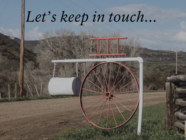 Photograph of a mailbox along dirt road under blue cloudless sky. Text reads "Let's keep in touch..."