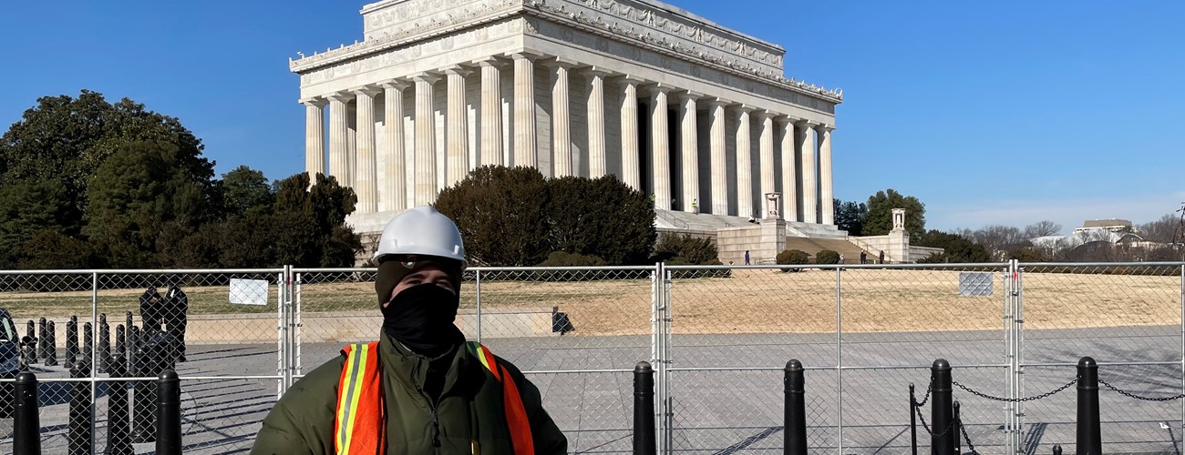 Ranger wearing a face mask and safety vest standing next to a fence near the Lincoln Memorial
