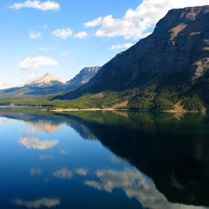 lt= A mountain in Glacier National Park is reflected in a still lake.