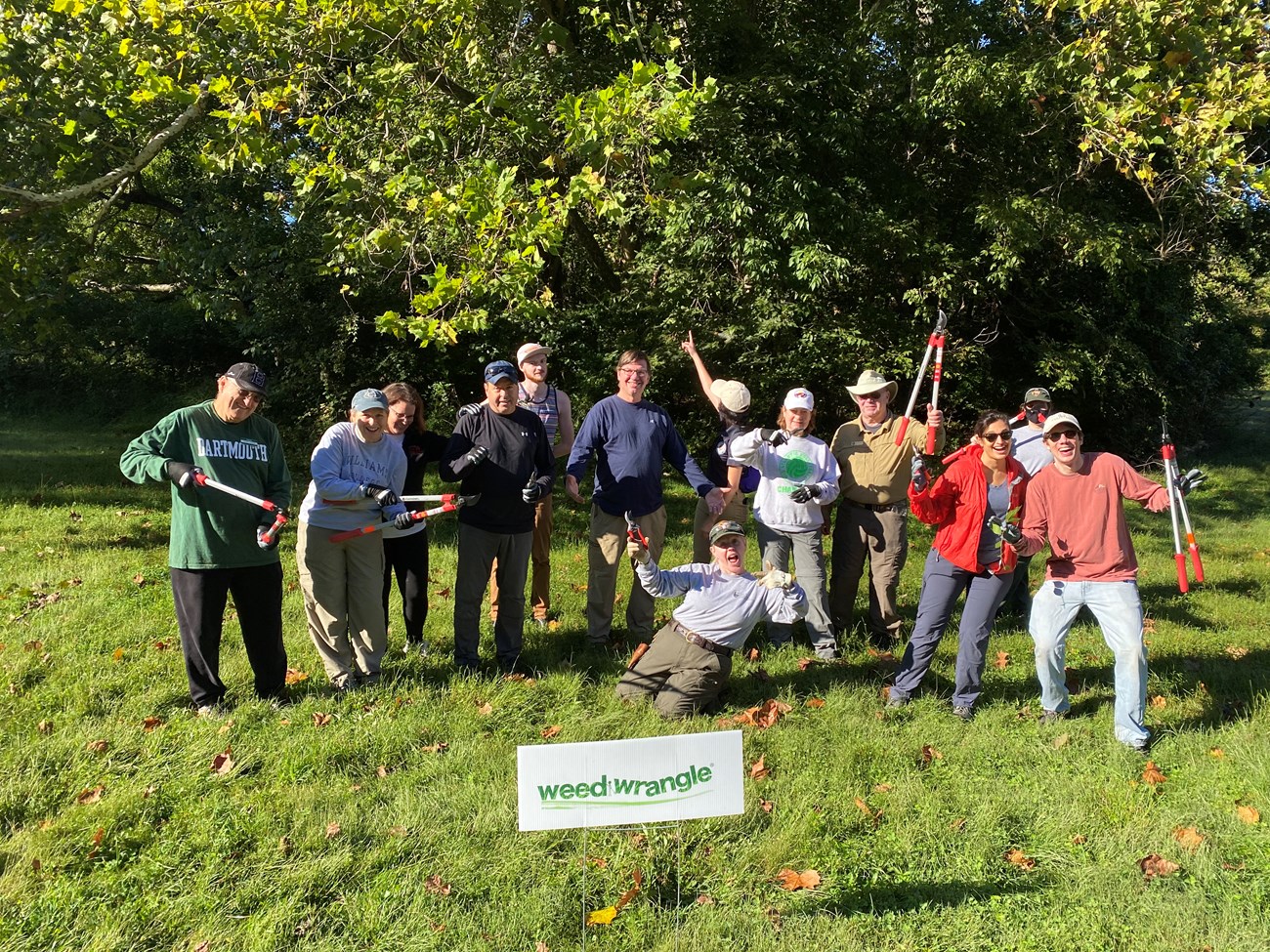 a group of people pose for a photo outdoors with a sign that says "weed wrangle"