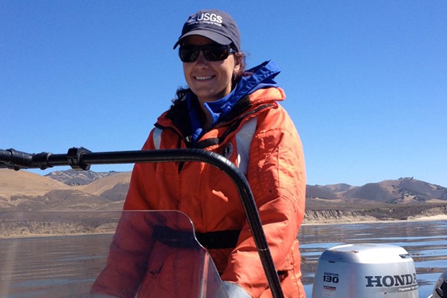 Woman driving boat on ocean with orange jacket.