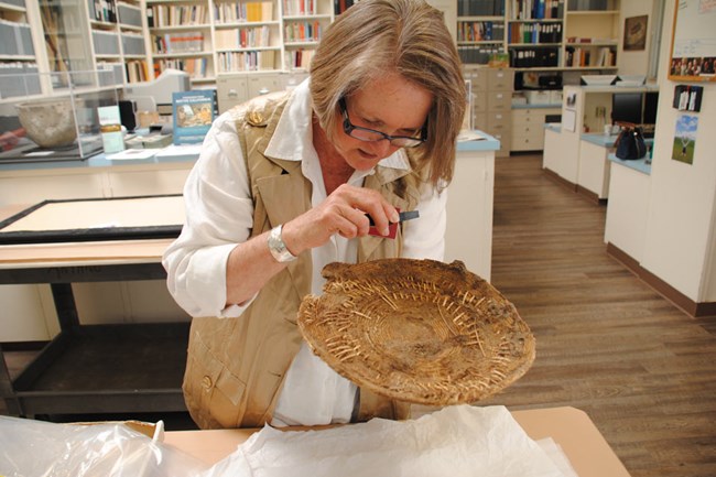 Woman examining artifact with magnifying device.