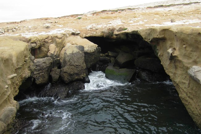 a small sea cave with ocean waves crashing against the entrance