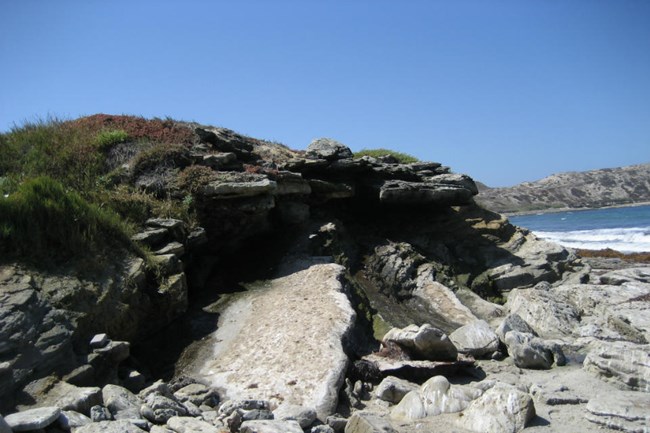 rocky mound next to the ocean with freshwater flowing out of an opening in the middle