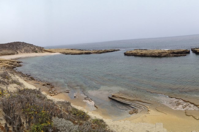 lt= a natural harbor with large rocks blocking the entrance and plants in the foreground