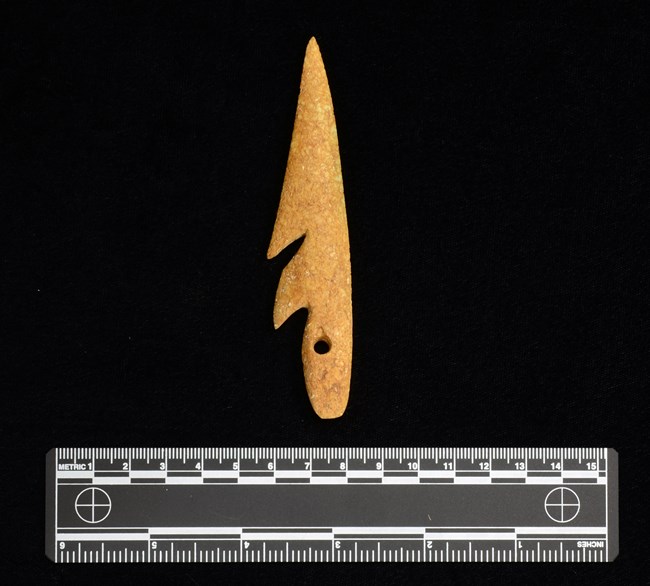 Carved fish hook on black background with ruler.