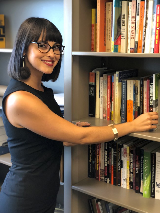 Young woman standing in front of a bookshelf.