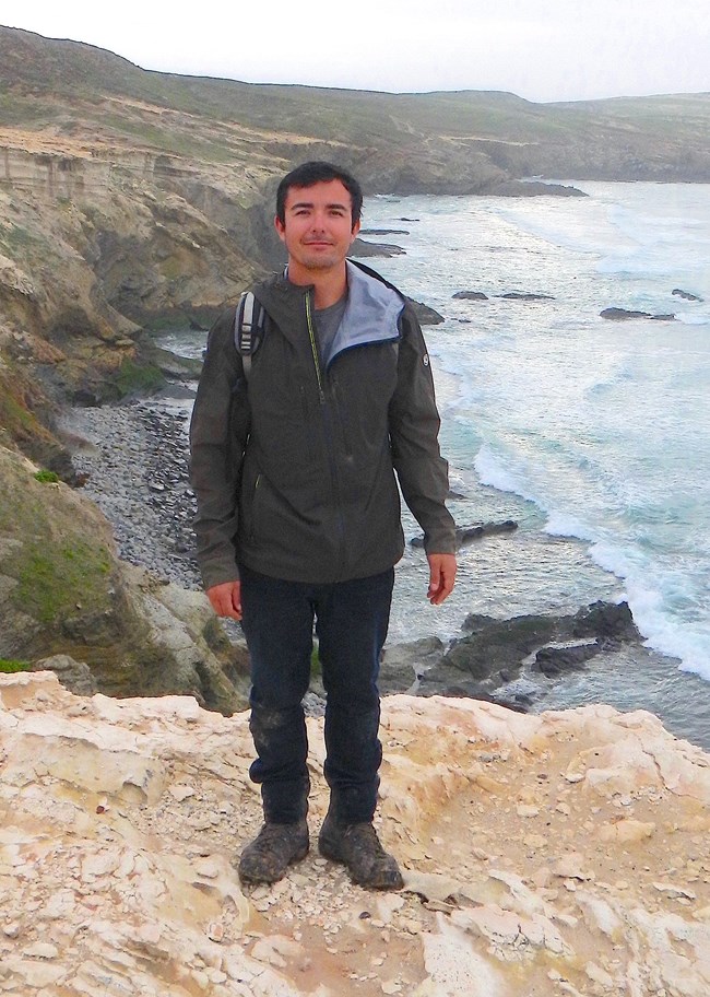 Young man on top of island cliff overlooking ocean