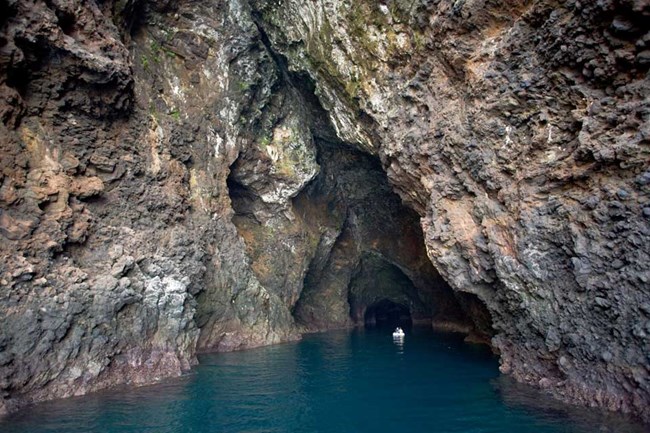 Sea cave with rust and black colored rocks and boat in the middle.