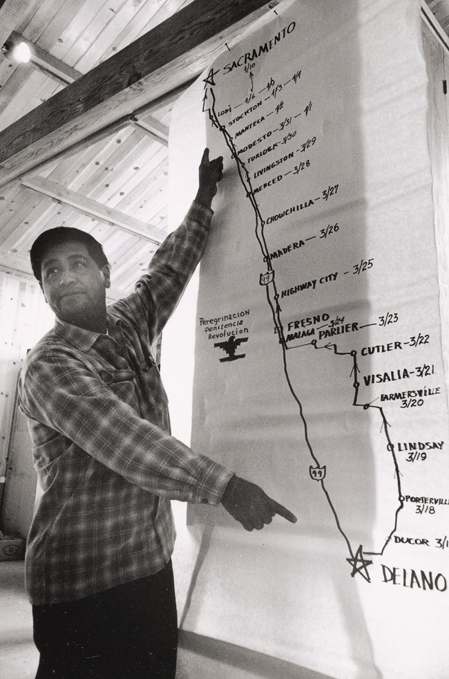 Image of César E. Chávez standing in front of a map with route of 1966 march.