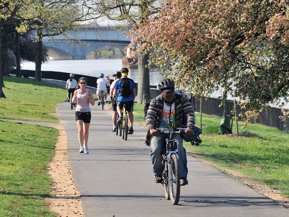Visitors ride bikes and jog down a paved path along a river in the Georgetown Waterfront Park during the springtime.