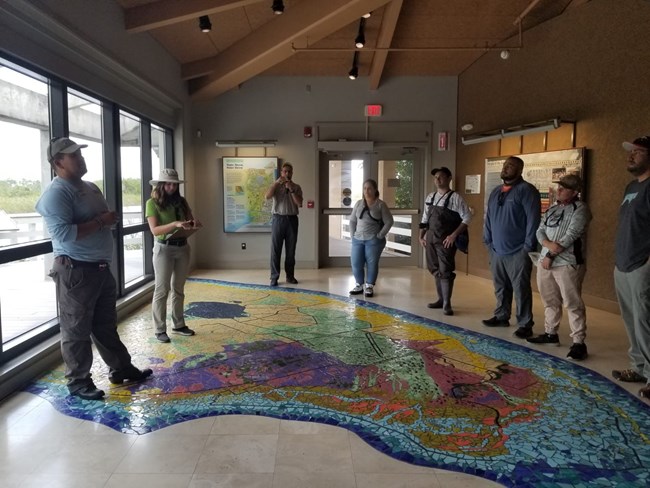 Eight people stand talkig around a large floor map.