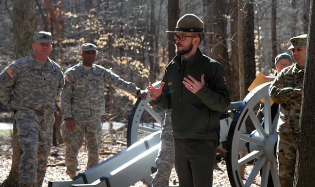 Park ranger shows people in military fatigues around Revolutionary War Cannon.