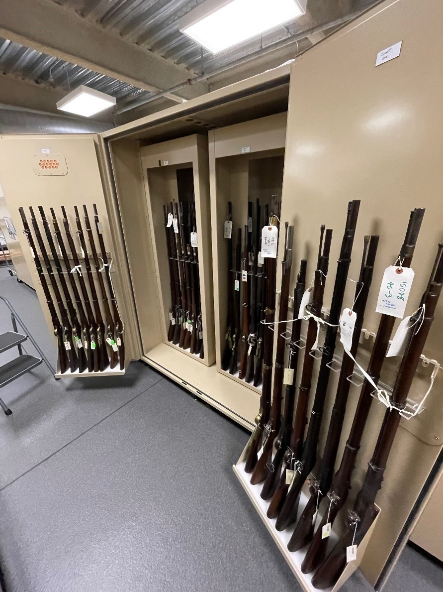 A large metal cabinet with two doors open to display historic firearms.