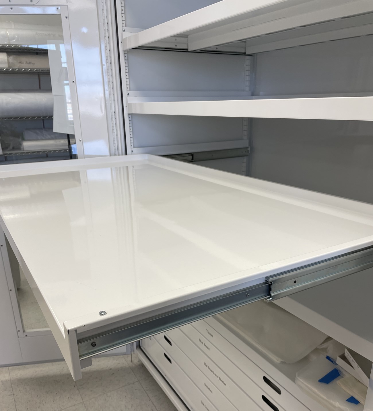 White museum cabinet with a single shelf pulled out to display the track mechanisms.