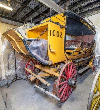 Side view of stage coach painted yellow with red painted spoke wheels. Black numbers, "1002," painted on side. Yellow letters, "Yellowstone" painted at top side of stagecoach. Side view of stage coach painted yellow with red painted spoke wheels. Black numbers, "1002," painted on side. Yellow letters, "Yellowstone" painted at top side of stagecoach.