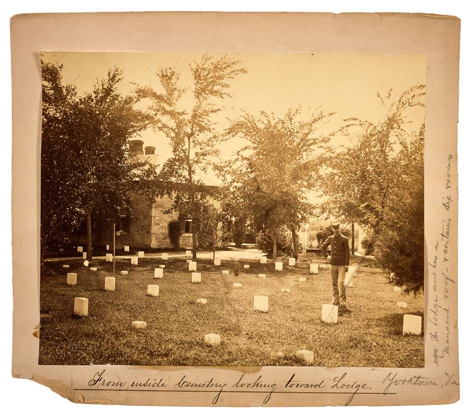 Yorktown National Cemetery Lodge, 1876-1877 A man in military uniform stands in turf among rows of marble headstones, with a stone lodge and trees in the background.