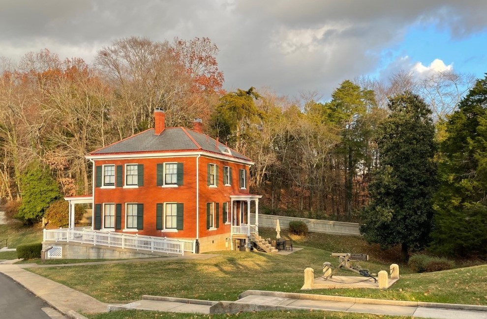 A two-story red-brick lodge with a slate roof beside the entrance drive of the national cemetery
