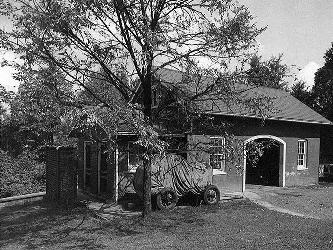 Andrew Johnson National Cemetery Stable, 1949 A tarp covered wagon and tree stand beside a brick stable, showing a restroom addition on the side.