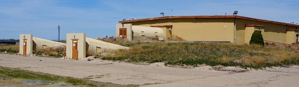 Mountain HomeAFB Ground Alert Facility Elmore County Idaho A yellow concrete building is low on the ground with doors coming from three tubes connected to one side.