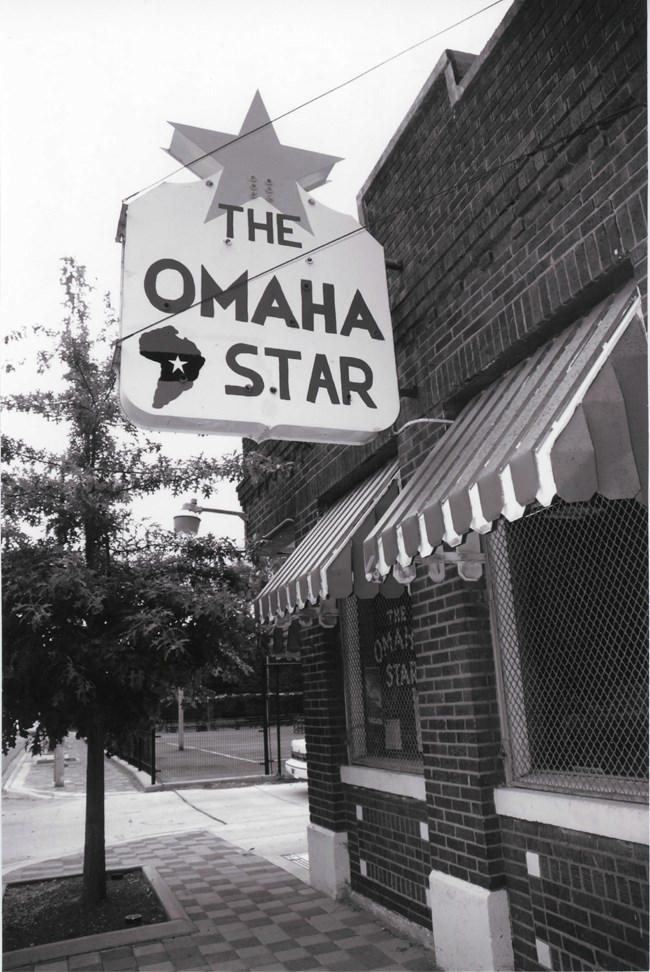 07001322-Omaha-Star Small brick building on street corner with large sign stating: The Omaha Star with an image of Africa in the sign