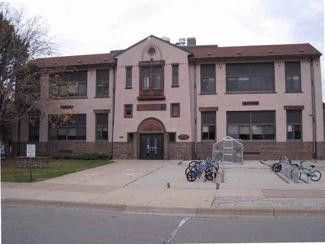 Front entrance to two-story school with pink hued cladding and arched entryway