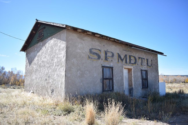 One-story rectangular (31’-9” x 20’) lodge hall or sala, has stuccoed adobe block walls atop a concrete foundation,