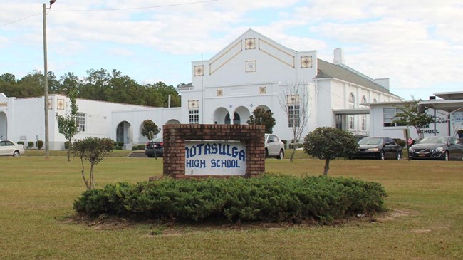 School building with a sign framed in brick in the for front lawn of the school with bushes