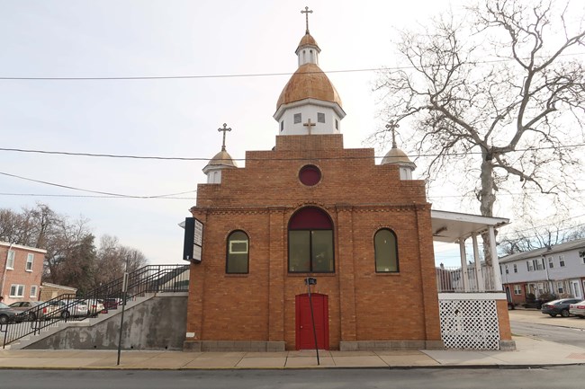 A tall, one-story, rectangular building with a raised, finished, full basement, and an asphalt-shingled roof with an arched-front brick vestibule and domed cupolas