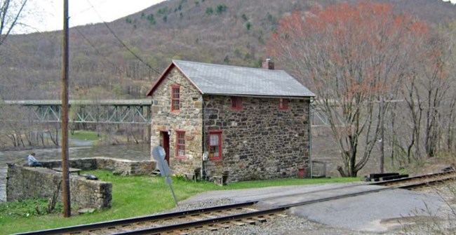 Two story stone cabin on river with bridge in background