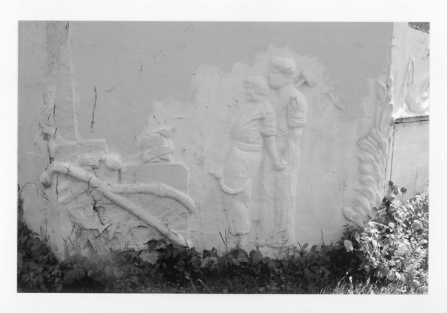10000813-GoldmanHouse-Photo4 Wall of bulding showing figurative bas-relief of a man and a woman